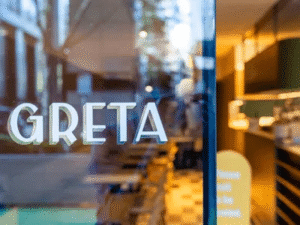 Restaurant window with "GRETA" signage and a view of the modern interior and street reflection.