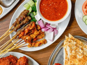 Plate of grilled meat skewers, dipping sauce, and flatbread served on a wooden restaurant table.
