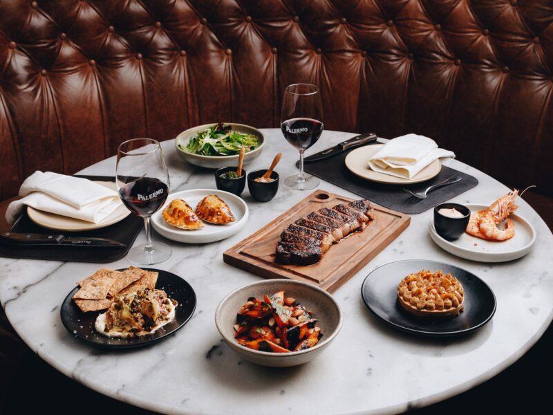 Dining table at Palermo Melbourne with steak, seafood, sides, desserts, and wine.